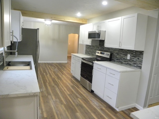 kitchen with beamed ceiling, appliances with stainless steel finishes, white cabinetry, backsplash, and dark hardwood / wood-style floors