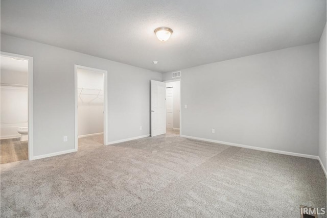 unfurnished bedroom with carpet flooring, a spacious closet, a textured ceiling, ensuite bath, and a closet