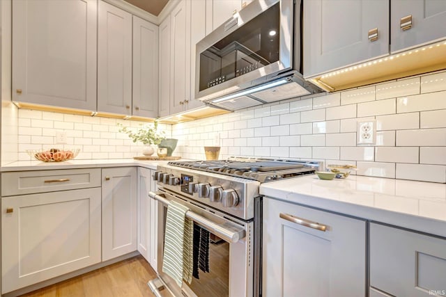 kitchen featuring light stone countertops, decorative backsplash, light wood-type flooring, white cabinets, and stainless steel appliances