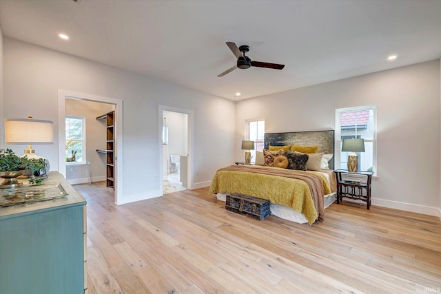 bedroom featuring ceiling fan, ensuite bathroom, light hardwood / wood-style flooring, and a walk in closet