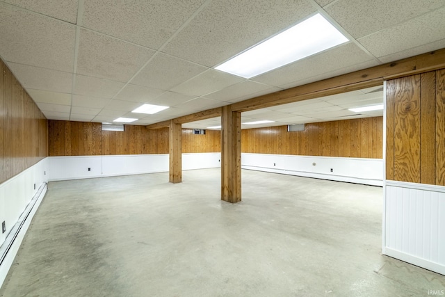 basement with a baseboard heating unit, a paneled ceiling, and wood walls