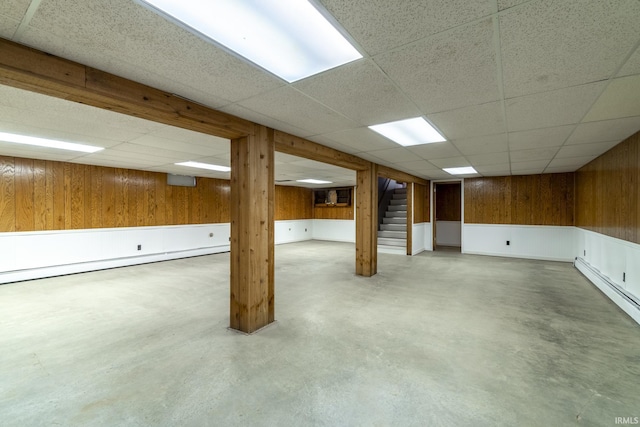 basement with baseboard heating, a paneled ceiling, and wood walls