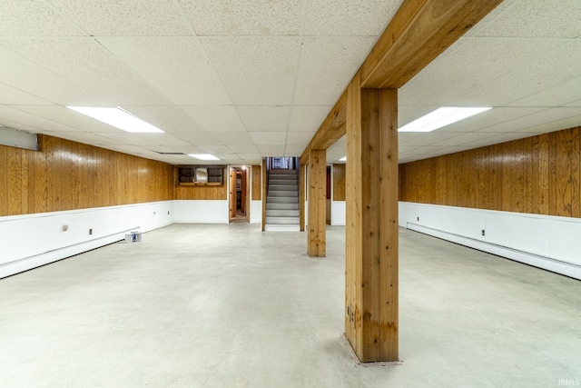 basement featuring baseboard heating, a drop ceiling, and wood walls