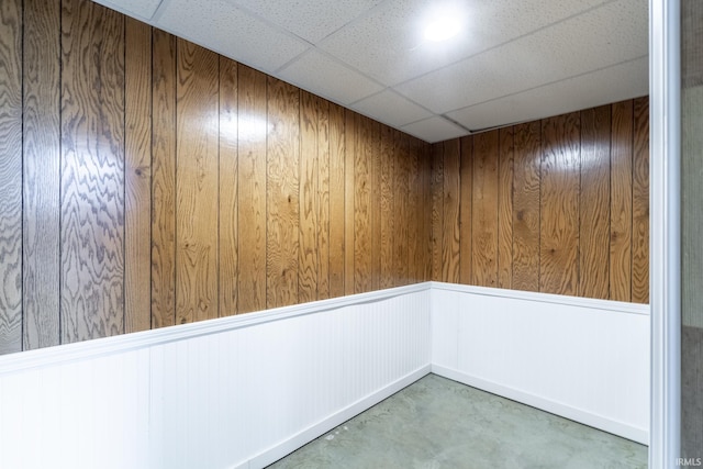 spare room featuring elevator, a paneled ceiling, wooden walls, and concrete flooring