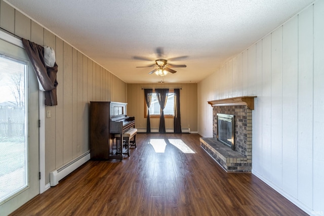 living room with a fireplace, a textured ceiling, baseboard heating, dark hardwood / wood-style flooring, and ceiling fan