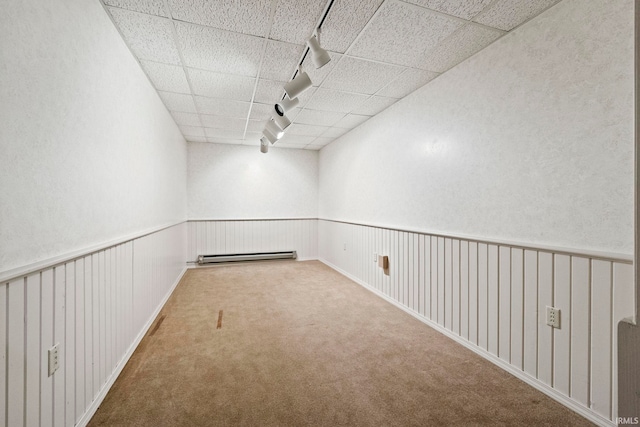 carpeted empty room featuring a baseboard heating unit and track lighting