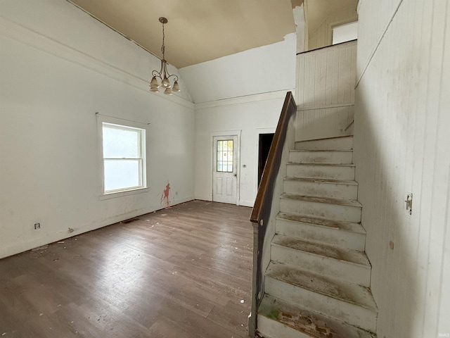 stairs featuring wood-type flooring, an inviting chandelier, and high vaulted ceiling