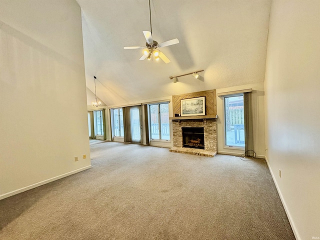 unfurnished living room with a brick fireplace, track lighting, ceiling fan with notable chandelier, carpet floors, and high vaulted ceiling