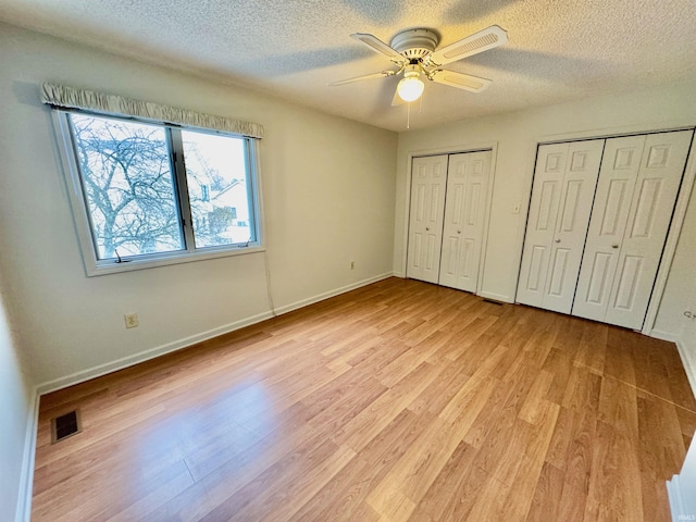 unfurnished bedroom featuring light hardwood / wood-style floors, a textured ceiling, two closets, and ceiling fan