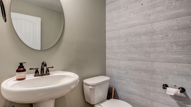 bathroom featuring sink, toilet, and wooden walls