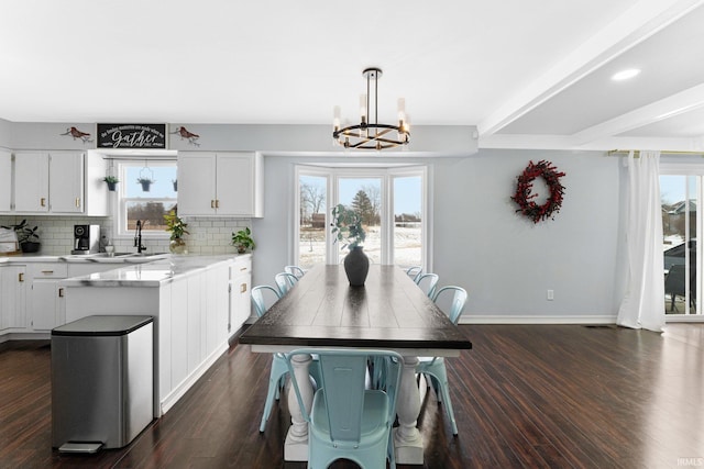 dining area featuring sink, a wealth of natural light, an inviting chandelier, and dark hardwood / wood-style flooring