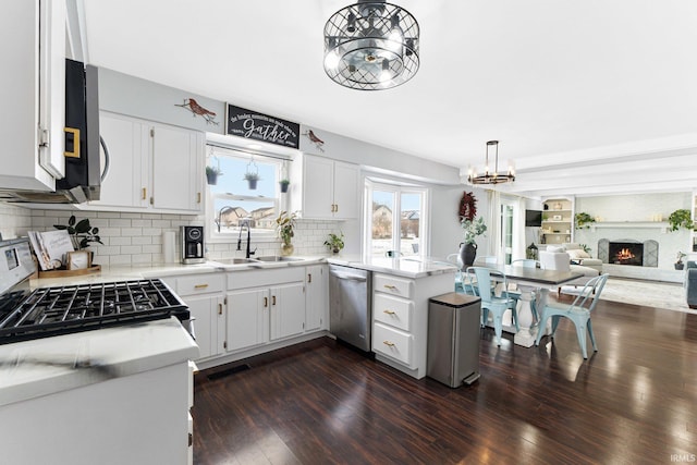 kitchen featuring white cabinets, appliances with stainless steel finishes, hanging light fixtures, a notable chandelier, and a brick fireplace