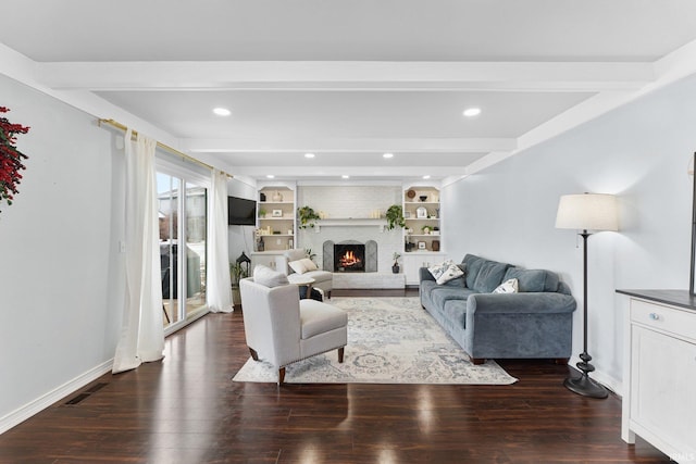 living room featuring built in features, dark wood-type flooring, beamed ceiling, and a brick fireplace