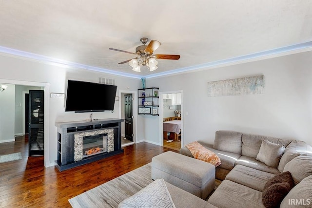 living room featuring ceiling fan, a stone fireplace, crown molding, and dark hardwood / wood-style flooring