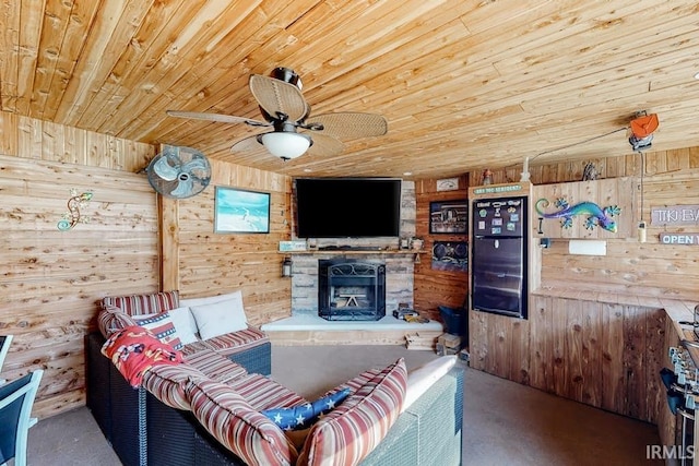 living room with ceiling fan, wood walls, a stone fireplace, and wood ceiling