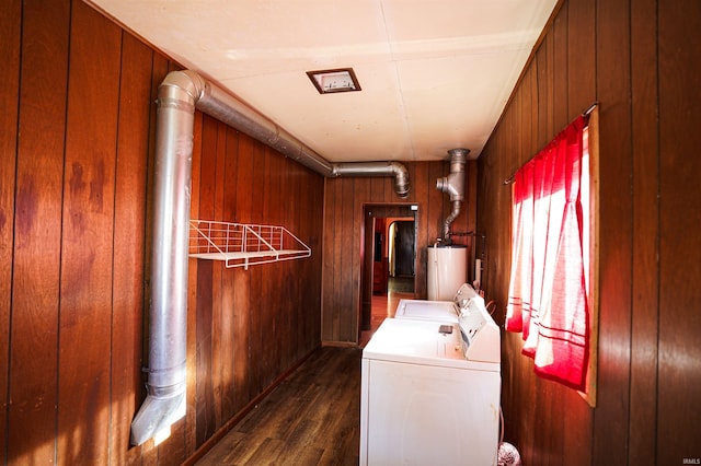 laundry room featuring water heater, dark hardwood / wood-style flooring, wood walls, and washing machine and dryer