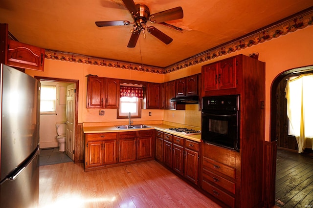 kitchen featuring white gas stovetop, sink, light wood-type flooring, black oven, and stainless steel fridge