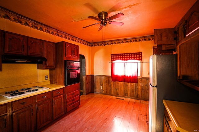 kitchen featuring stainless steel fridge, oven, light wood-type flooring, ceiling fan, and white gas cooktop