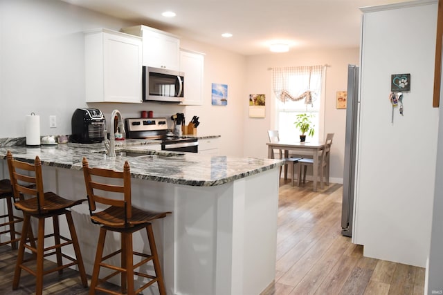 kitchen featuring white cabinets, kitchen peninsula, appliances with stainless steel finishes, and stone countertops