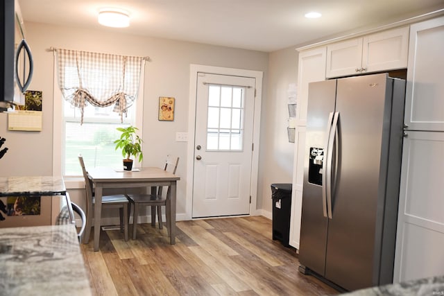 kitchen with stainless steel refrigerator with ice dispenser, white cabinetry, light hardwood / wood-style flooring, and light stone countertops