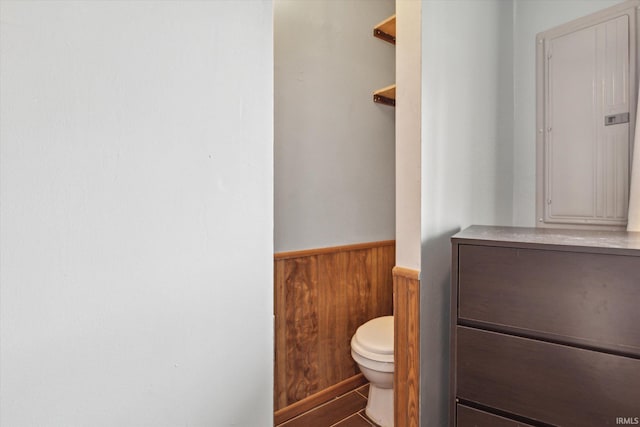 bathroom with electric panel, wood walls, and toilet