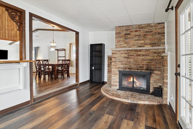 living room with a paneled ceiling, a fireplace, and dark hardwood / wood-style flooring