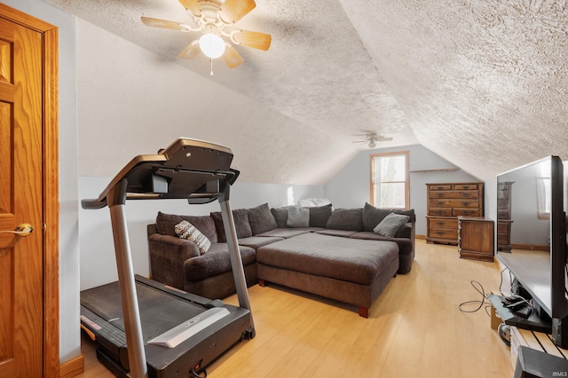 workout room featuring ceiling fan, vaulted ceiling, light hardwood / wood-style floors, and a textured ceiling