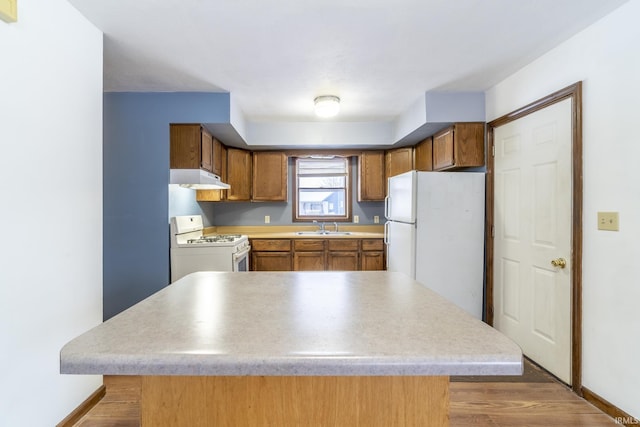 kitchen featuring sink, white appliances, wood-type flooring, and a kitchen island