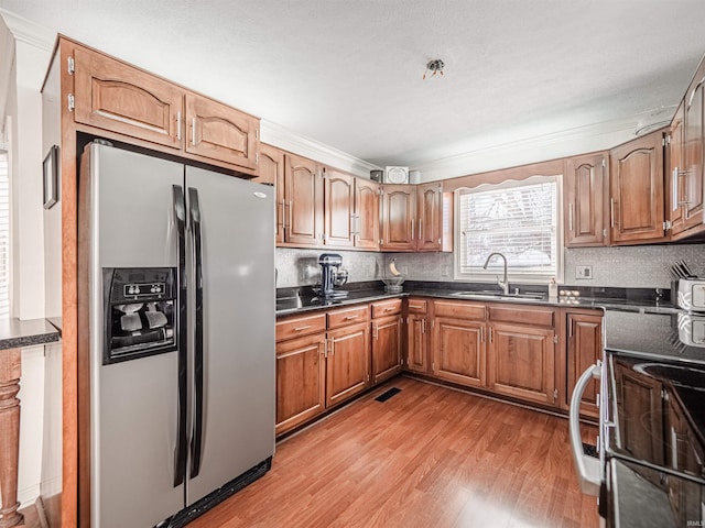 kitchen featuring sink, ornamental molding, range, light hardwood / wood-style floors, and stainless steel refrigerator with ice dispenser