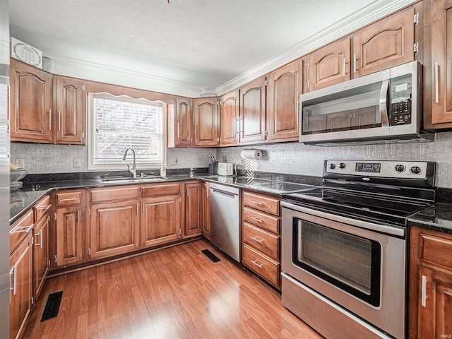 kitchen featuring sink, tasteful backsplash, light hardwood / wood-style flooring, dark stone counters, and stainless steel appliances