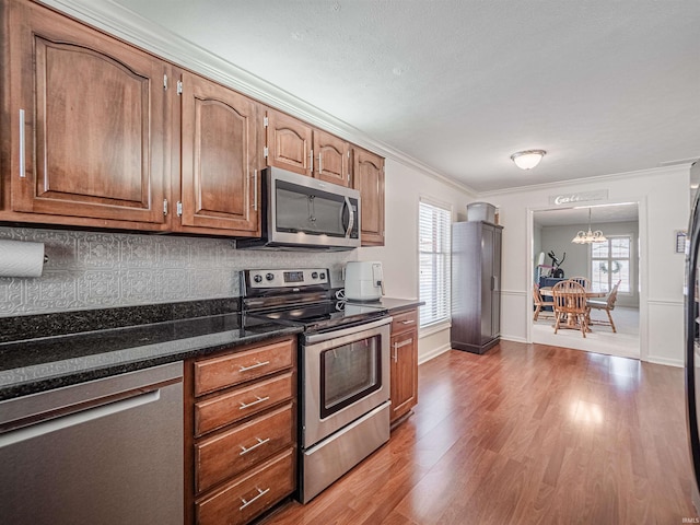 kitchen featuring appliances with stainless steel finishes, decorative backsplash, hardwood / wood-style flooring, crown molding, and an inviting chandelier