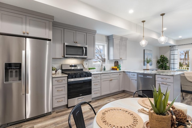 kitchen featuring gray cabinets, stainless steel appliances, light stone countertops, light hardwood / wood-style floors, and backsplash