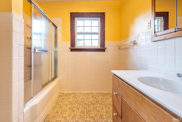 bathroom with tile walls, vanity, and bath / shower combo with glass door