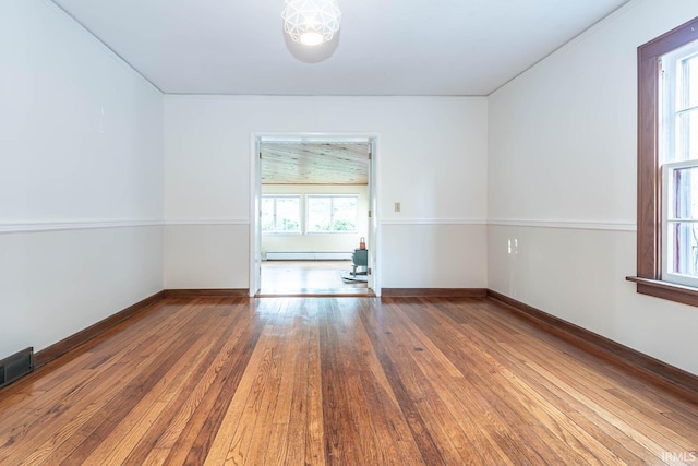 empty room featuring wood-type flooring and a baseboard heating unit