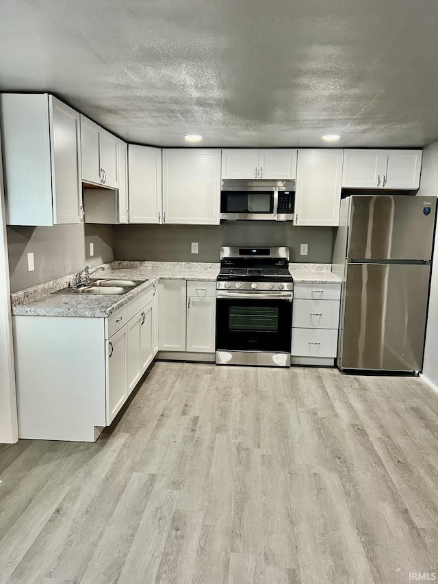 kitchen featuring sink, light hardwood / wood-style floors, white cabinets, and appliances with stainless steel finishes