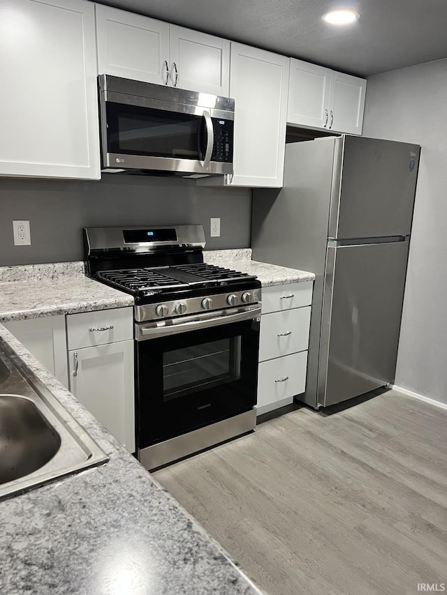 kitchen featuring appliances with stainless steel finishes, sink, light hardwood / wood-style flooring, and white cabinets