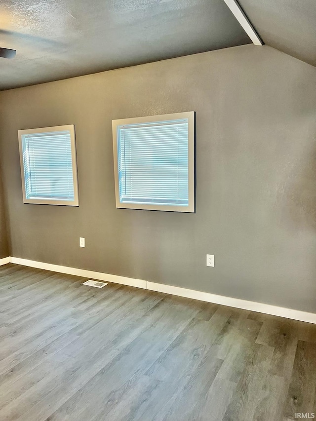 empty room featuring vaulted ceiling, plenty of natural light, a textured ceiling, and light hardwood / wood-style flooring