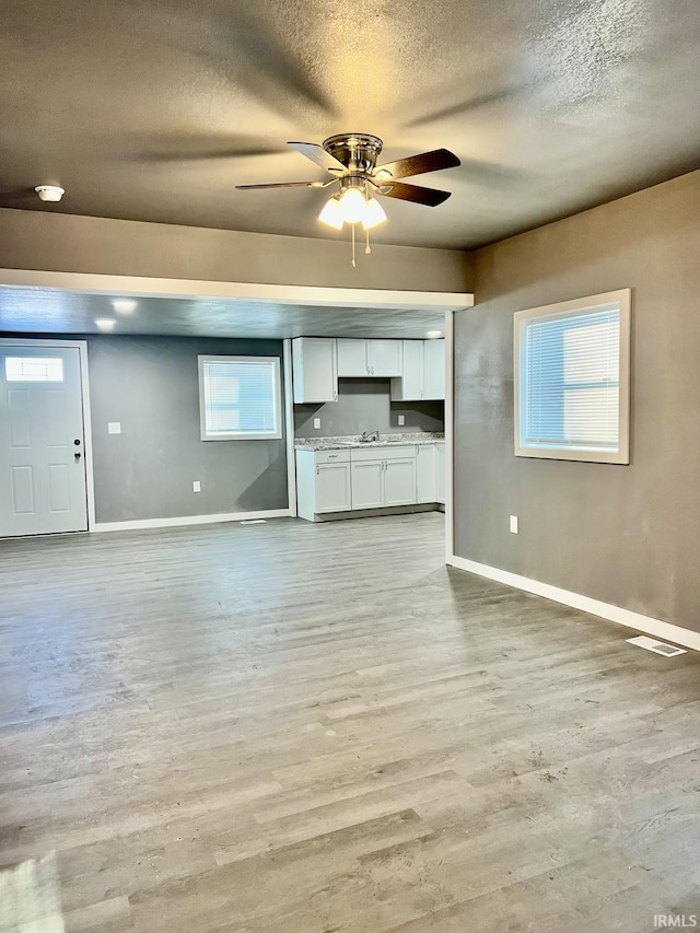 unfurnished living room featuring ceiling fan, sink, light hardwood / wood-style floors, and a textured ceiling