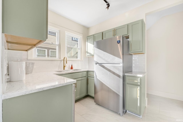 kitchen featuring light stone counters, decorative backsplash, stainless steel refrigerator, and green cabinetry