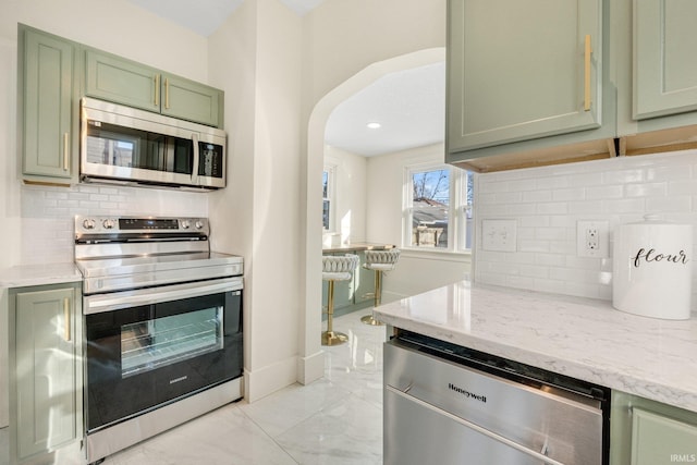 kitchen featuring appliances with stainless steel finishes, light stone countertops, green cabinets, and backsplash