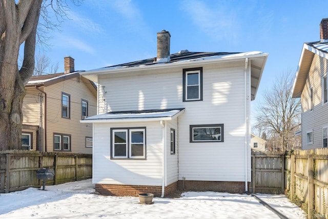 snow covered rear of property featuring solar panels