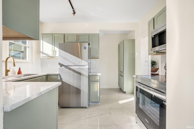 kitchen with sink, green cabinetry, appliances with stainless steel finishes, light stone countertops, and decorative backsplash