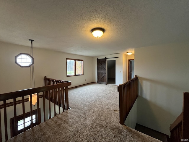 corridor with carpet floors, a barn door, and a textured ceiling