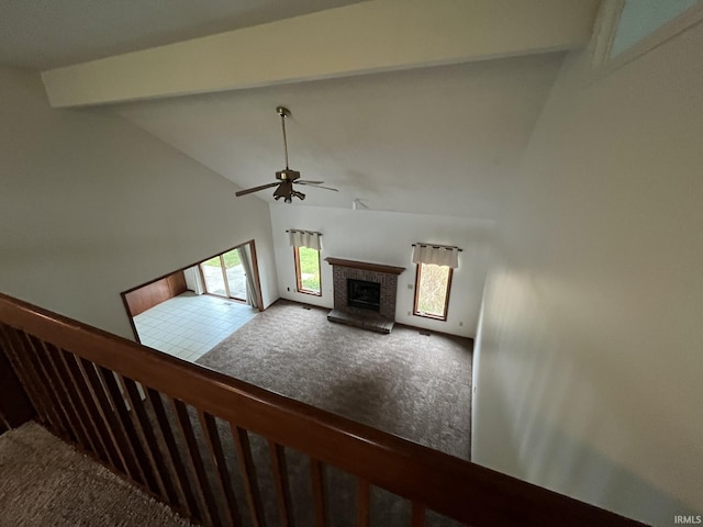 unfurnished living room with ceiling fan, high vaulted ceiling, carpet, a fireplace, and beamed ceiling