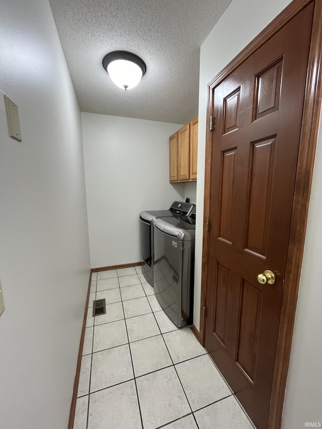 clothes washing area featuring cabinets, washing machine and dryer, a textured ceiling, and light tile patterned floors