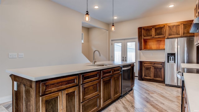 kitchen with sink, light hardwood / wood-style flooring, appliances with stainless steel finishes, a center island with sink, and decorative light fixtures