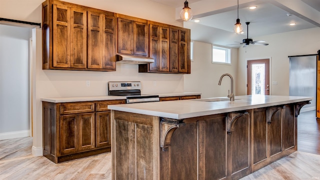 kitchen with sink, stainless steel electric range, a barn door, and a center island with sink