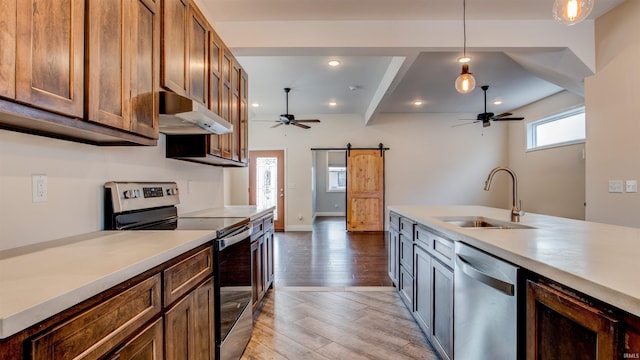 kitchen featuring sink, pendant lighting, stainless steel appliances, a barn door, and light hardwood / wood-style floors