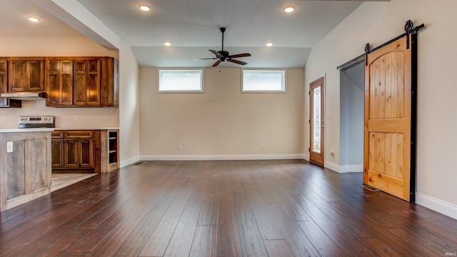 unfurnished living room with dark hardwood / wood-style floors, ceiling fan, a barn door, and vaulted ceiling