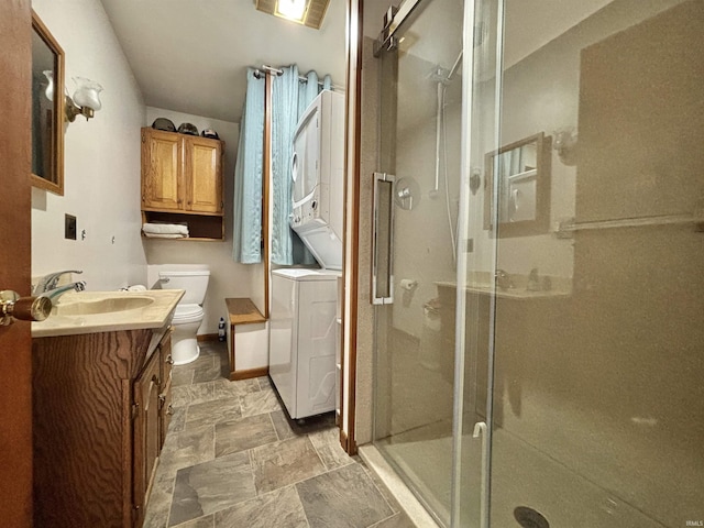 bathroom with vanity, a shower with shower door, stacked washer / drying machine, and toilet